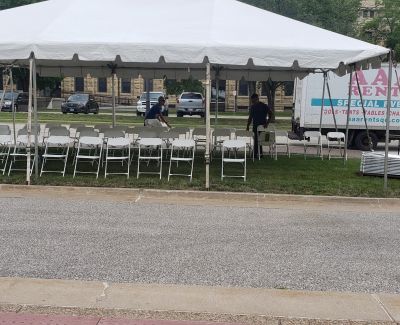 White folding chairs arranged in rows under a white tent beside a road, with an AAA Rents QC truck and staff setting up nearby.