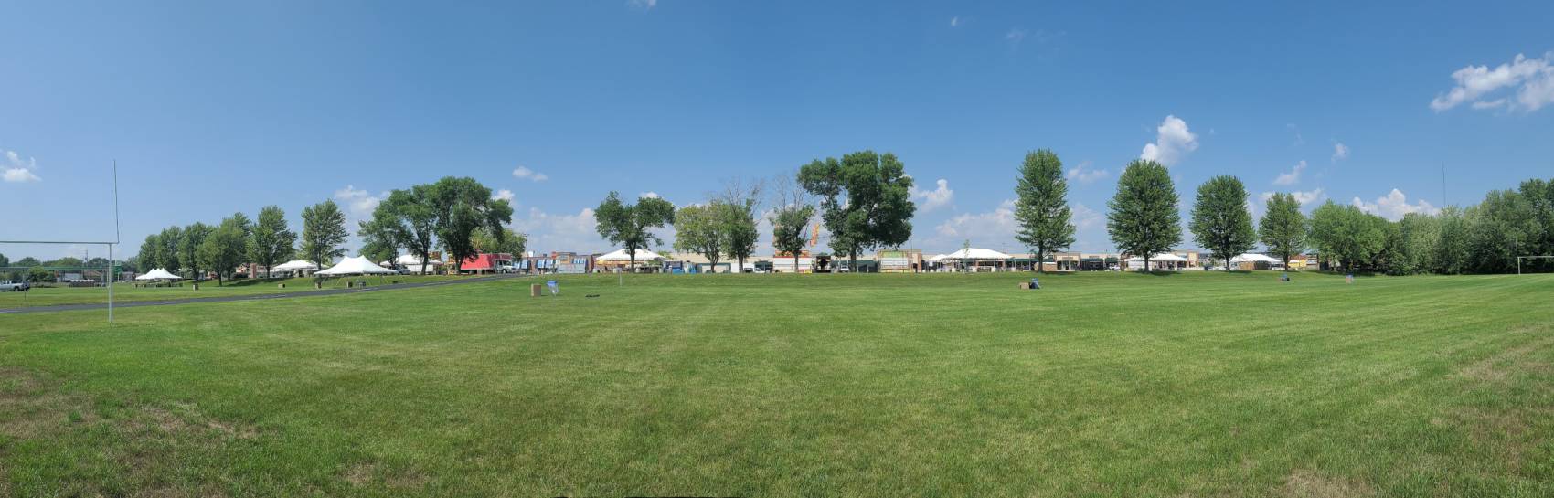 A spacious green view of a field with an event being set up in the background.