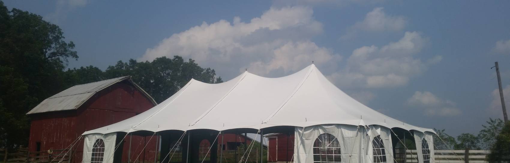 A tent being set up for a small event outside near a red barn.