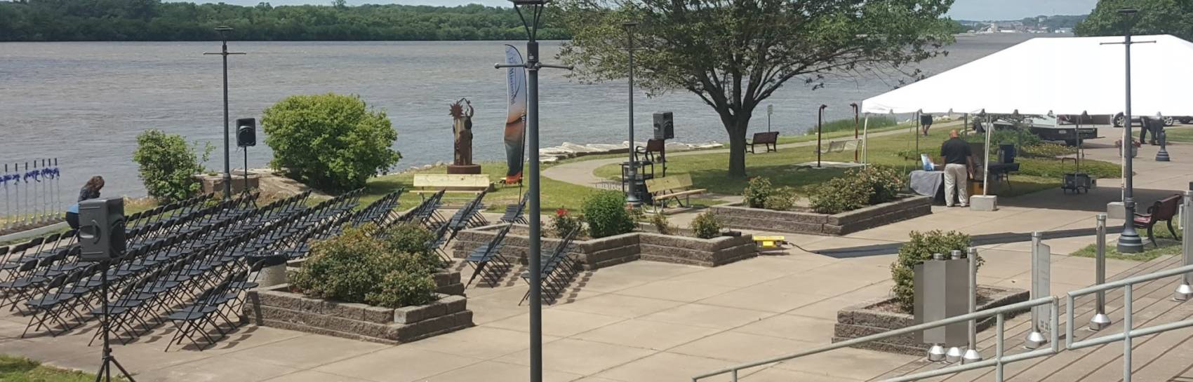 An outdoor event set up against a river with speakers and tents.