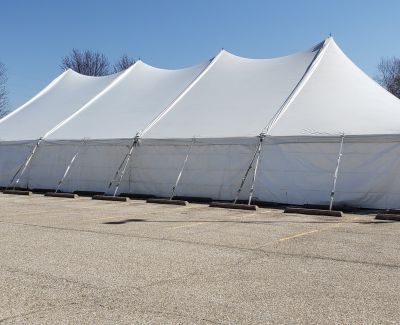 A side profile view of the large multi-peak white Century-style tent set up in an empty asphalt parking lot, showing the full length and multiple high peaks.