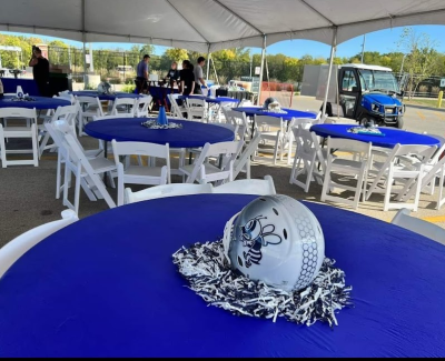 Close-up of a round table under an event tent, covered with a blue cloth and featuring a centerpiece.