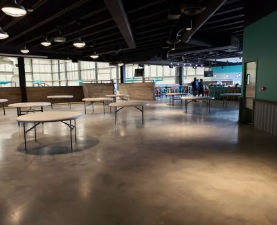 An indoor common area or food court with polished concrete floors, featuring several empty round pedestal tables spaced throughout the room.