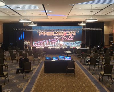 A large conference room or ballroom set up theater-style with chairs facing a stage dominated by a large LED screen displaying 