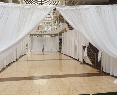 An elegant entrance corridor created using white pipe and drape, with the drapes pulled back like curtains at the opening, leading down a tiled pathway