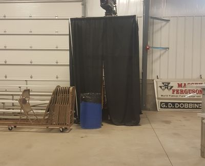 A section of a warehouse or loading dock area partitioned off with black pipe and drape, next to stacked folding chairs on a dolly.