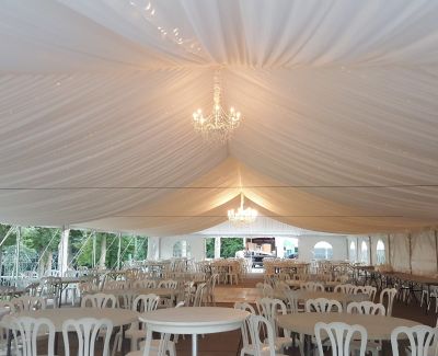 White event tent with draped ceiling and chandeliers, featuring round tables and white chairs arranged for a reception