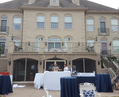 Outdoor reception area in front of a large brick house with string lights and cocktail tables dressed in navy linens.