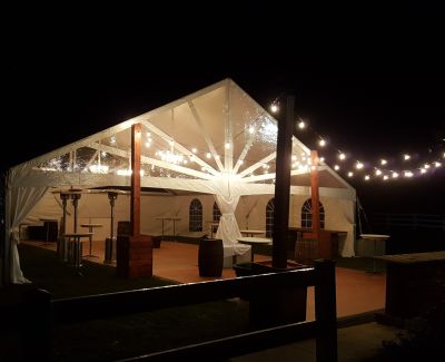 Nighttime outdoor wedding tent with string lights and a cozy rustic ambiance featuring barrels and patio heaters