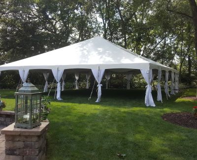 Square white canopy tent with draped corners set in a wooded garden area for an outdoor event.