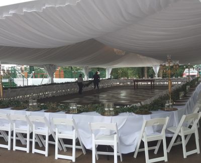 Large reception tent with draped white ceiling, long banquet tables in a square layout, and a central dance floor