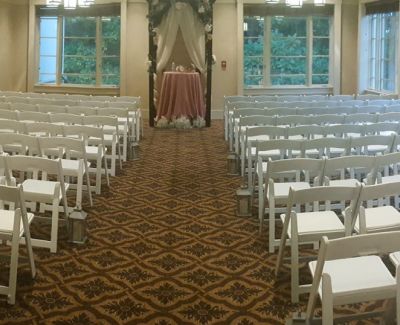 Indoor ceremony space with white folding chairs arranged in rows facing a small altar beneath a floral arch.