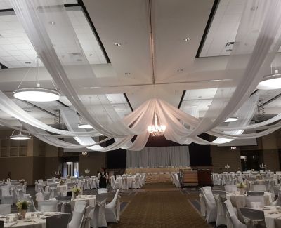 A indoor wedding event being held with round tables and white draping ceiling decorations.