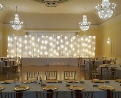 A indoor wedding ceremony being held with chandeliers around a rectangular table set up.