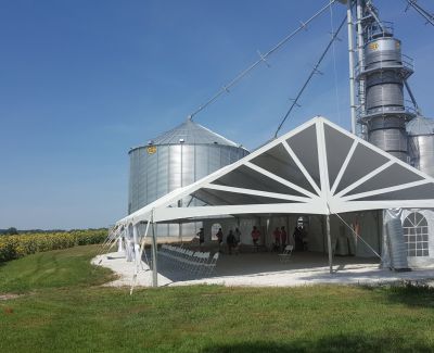 A outdoor tent with windows being held near some outdoor barn equipment.