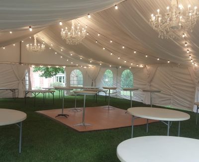 An indoor tent with hanging lights over round tables being set up.