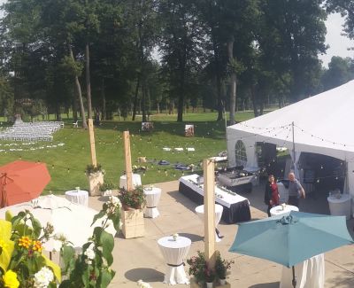 Outdoor cocktail area with umbrellas and high-top tables near a large white tent in a grassy venue.