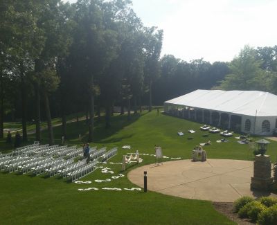 Wide view of a grassy outdoor wedding ceremony space with white chairs set up in front of a large event tent.