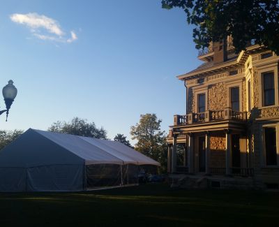 Historic house with a white event tent set up on the lawn during sunset.