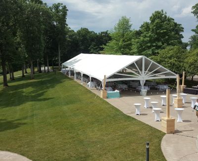 Large open white tent on a sloped grassy area with cocktail tables and string lights.